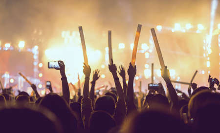 Silhouette crowd of concert stage lights and people fan audience raising hands or glow stick in the music festival rear view の写真素材