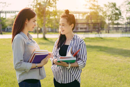 Young women together study reading book in university and knowledge at outside or park campus relaxing smile in summer seasonの写真素材
