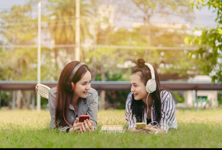 Young women teenagers together student listening music with headphone university college outdoor with school folder and relaxing having fun enjoy or study online conceptの写真素材