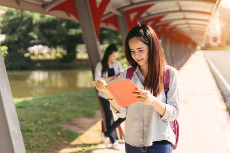 Young women students together study reading book in university and knowledge at outside or park campus relaxing smile in summer seasonの写真素材