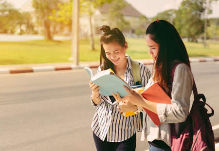 Young women students together study reading book in university and knowledge at outside or park campus relaxing smile in summer seasonの写真素材