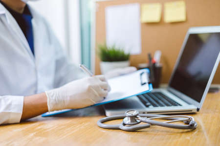 Doctor with stethoscope writing note result in hospital concept - clinic heath care equipment tool in lab with laptop computerの写真素材
