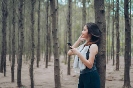 Asian woman listening music in the forest afrer runner workout cadio with smartphone and earphone her relaxing and enjoy happy healthy lifestyle freedom.の写真素材