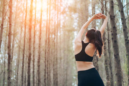 Asia woman sporty resting relax muscles in the forest after runner cardio exercise workout, female happy enjoying freedom active healthy lifestyle stretching on summer at mountain rear view.の写真素材