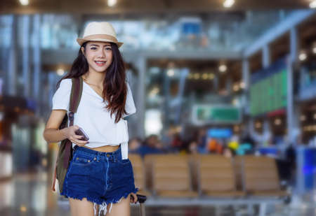 Asian woman teenager using smartphone walking at airport terminal with luggage suitcase and backpack...