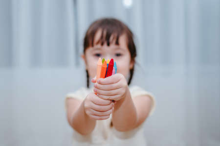 A Kid girl holding crayons paints and drawing for skills before kindergarten or preschool,children education and knowledge at home.の写真素材