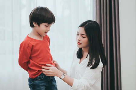 Mother dressing up a son for beginner school lessen and first day at room to going kindergarten education, parent protection boy concept. の写真素材