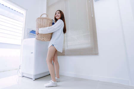 woman asian doing housework or chores with washing machine laundry holding basket for loading clothes and in the room, happy housekeeping everyday concept.の写真素材