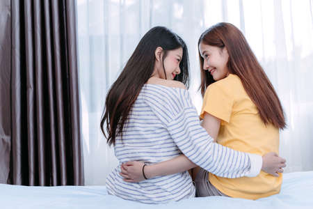 Same sex asian lesbian couple lover embrace in the bedroom at morning happiness feeling, LGBT sexuality female hug sitting and living together at home rear view.の写真素材