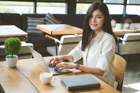 Freelancer asian woman working job using digital laptop computer and drink coffee breakfast on workplace table at cafe shop.の写真素材