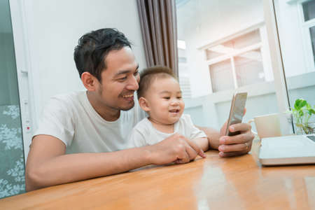 Asian father and little son watching video from smartphone at home happiness laughing together,...