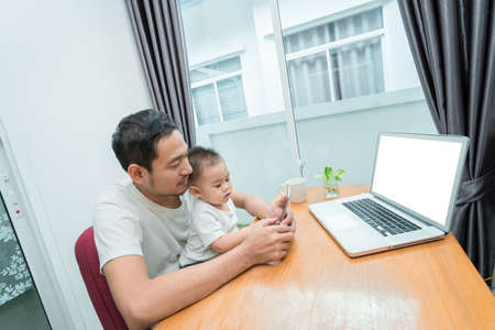 Asian father and little son watching video from smartphone at home happiness laughing together, happy family concept.の写真素材