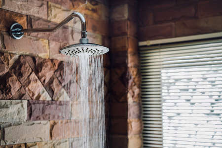 Shower in bathroom flowing water drop to the floor at modern home of brick style near windowの写真素材