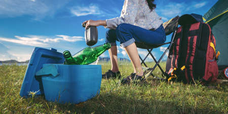 Asian woman camping and backpack travel sitting relax alone with drinks beer,water for refreshing active at morning having happy lifestyle nature mountain in forest.の写真素材