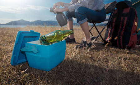 Asian woman camping and backpack travel sitting relax alone with drinks beer,water for refreshing active at morning having happy lifestyle nature mountain in forest.の写真素材