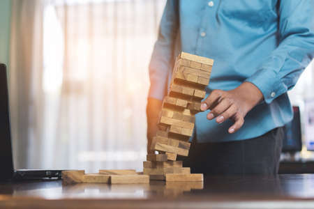 Businessman picking wooden block fail danger tower hands holding challenge game building construction protect plan and project for control risk shape.の写真素材