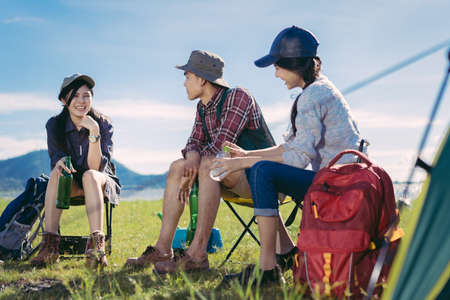 Asian group friends travel camping together in forest with backpack and tent picnic drinks beer,water at nature outdoor young teenager talking relax,rest near mountain view.の写真素材