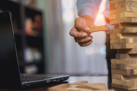Hand of businessman pulling wooden block before fail on building tower at home and drape change, choice business risking dangerous project plan failure constructionの写真素材