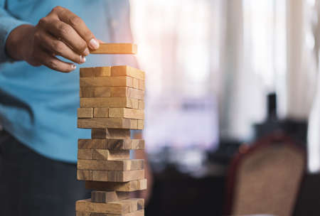 Hand of businessman pulling wooden block before fail on building tower at home and drape change, choice business risking dangerous project plan failure constructionの写真素材