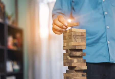 Hand of businessman pulling wooden block before fail on building tower at home and drape change, choice business risking dangerous project plan failure constructionの写真素材