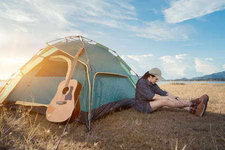 Asian woman camping and backpack travel sitting near tent relax alone with guitar at morning...