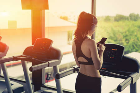 Woman exercise running workout listening music with headphone using smartphone with cardio and healthy lifestyle and bodybuilding at fitness gym rear view at morning.の写真素材