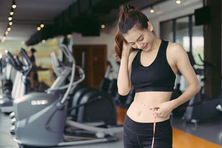 Young beautiful woman athlete using body fat measurement and waist size with waist line after...