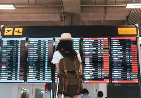 Asian woman traveler looking information board with carrying, suitcase luggage and passenger for...