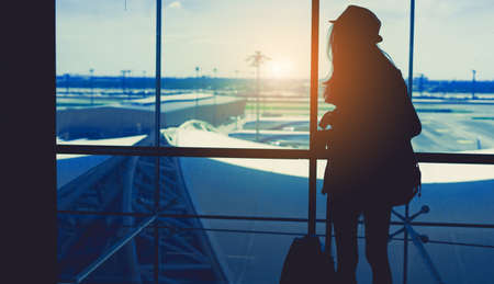 Silhouette woman travel with luggage looking without window at airport terminal international or girl teenager traveling in vacation summer relaxation holding suitcase and backpackの写真素材