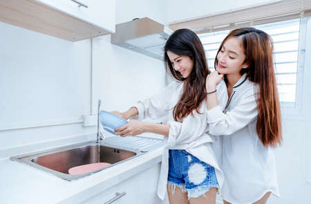 Same sex Asian Lesbian couple women asian doing housework or chores helping with washing dishs cleaning after breakfast in the morning, relationship female living together.の写真素材