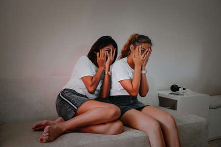 Mom and teenage daughter watching television horror scary  movie and eating chocolate bar on sofa at home in living room, Happy family together.の写真素材
