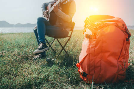 Backpack of woman playing guitar resting outdoor in trekking at sunset happiness.