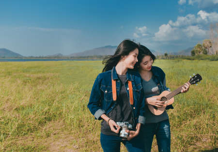 Friendship of Asian teenager women resting outdoor with camera and ukulele her playing music relax.
