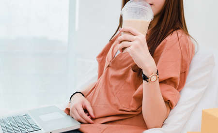 Closeup woman drinking cold coffee and using laptop computer business sme at home, Copy space.の写真素材
