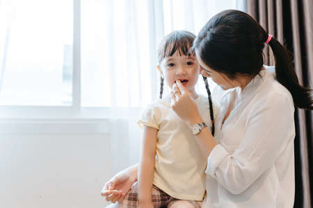 Mother feeding snack to daughter eating in the morning at home side window funny family together...