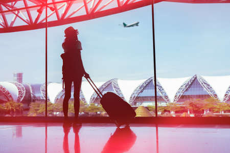 Silhouette woman travel with luggage looking without window at airport terminal international or girl teenager traveling in vacation summer relaxation holding suitcase and backpackの写真素材