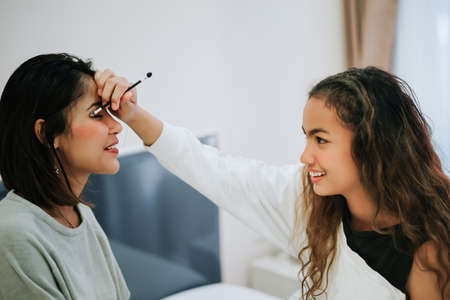 Happy Family teenage daughter is makeup to the mother in the bedroom in the morning before working.
