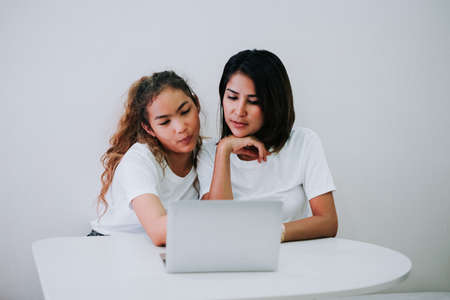Happy family Mom and teenage daughter using laptop computer helping together business or studying education at home.の写真素材