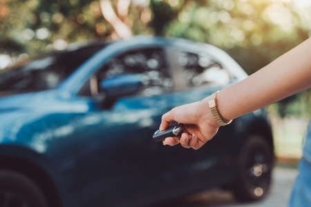 Close up hands woman pressing remote systems key near car for lock,unlock of blue hatchback car near street road driving.の写真素材
