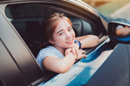 Asian woman smiling with Hatchback car travel driving road trip summer vacation in blue car at sunset,Girls happy traveling enjoy holidays and relaxation get the atmosphere and go to destinationの写真素材