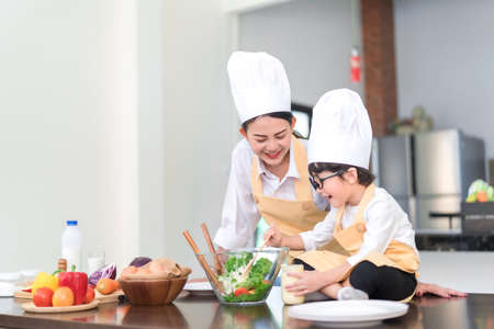 Professional Chef asian mom teaching little son cooking salad vegetable prepare healthy food in the kitchen room for dinner at home happy family lifestyle.の写真素材