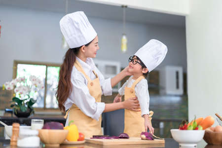 Professional Chef asian mom dressed up little son ready teaching cooking salad vegetable knowledge prepare healthy food in the kitchen room for dinner at home happy family lifestyle.の写真素材