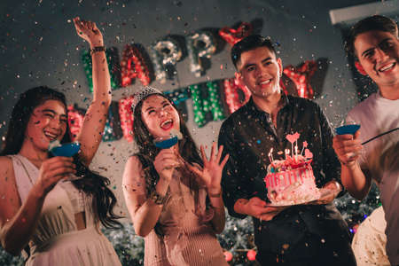 Asian woman birthday party friends big surprise burning candle with birthday cake and drinking cocktail throwing confetti happy together laugh celebrate.の写真素材