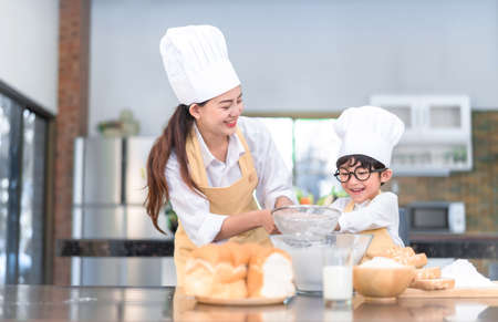 Happy family asian mom and son making bakery cake prepare delicious sweet food in the kitchen room...