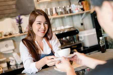 Professional Asian woman Barista preparing coffee at front counter serving coffee cup to customer occupation, part-time, job or owner business working woman happy selling and making drink beverageの写真素材