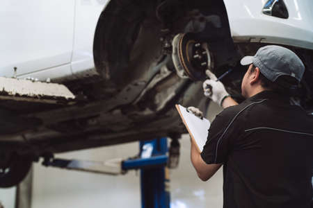 Mechanic asian man examining and service maintenance the suspension of a vehicle, Safety inspection test engine before customer drive a car on a long journey, transportation serviceの写真素材