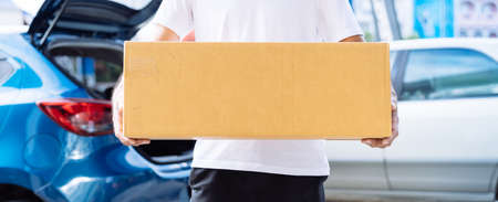 Delivery man carrying cardboard box for sending deliver to customer by transportation system hatchback car, Business of male transport sell part or product service parcel for convenience of customerの写真素材