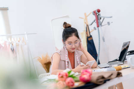 Beautiful asian woman fashion designer tailor fabric working and sewing her service clothes to customer, creative design in studio tailor shop, occupation owner small business conceptの写真素材