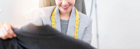 Beautiful asian woman fashion designer tailor fabric working and sewing her select clothes, creative design in studio tailor shop, occupation owner small business, copy space bannerの写真素材