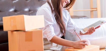 Working woman sme business at office in home interior her checking order from tablet for customer and online delivery for ready packing in bedroomの写真素材